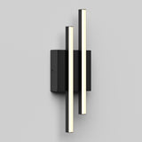 A modern wall sconce featuring two vertical, cylindrical LED light bars mounted on a rectangular black base, set against a plain light gray background.