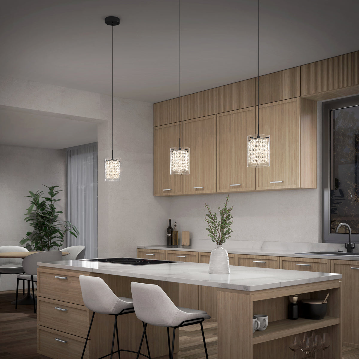 A modern kitchen with light wood cabinets, a white island with two cushioned bar stools, pendant lights hanging above, a vase with greenery on the countertop, and a window above the sink.