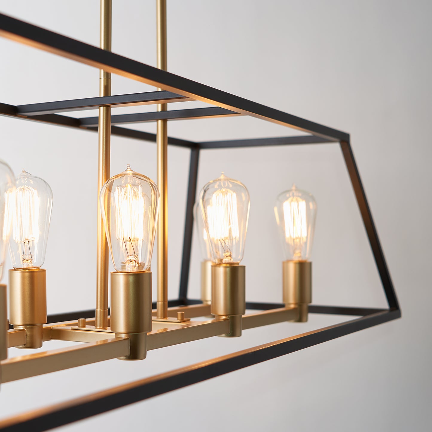 A close-up of the Artika Carter Long 8-light Chandelier, featuring exposed Edison-style bulbs and gold fixtures, suspended from the ceiling against a plain light background.