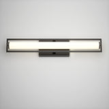 A modern, wall-mounted light fixture with a long, horizontal frosted glass tube and a black metal frame, illuminated against a plain white wall.