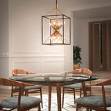 A modern dining room with a round glass table, four wooden chairs with gray cushions, a mug and magazine on the table, and a geometric gold chandelier above. Light wood floors and white paneled walls complete the space.