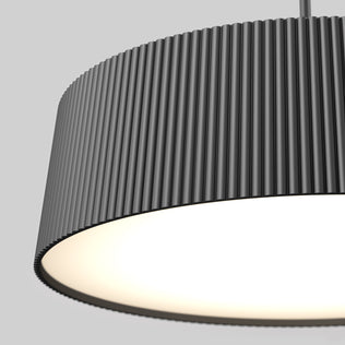 Close-up of the Artika Groove Drum LED contemporary pendant light 3 CCT, a modern black ribbed cylindrical lamp hanging from the ceiling, illuminated and casting a warm glow against a plain grey background.
