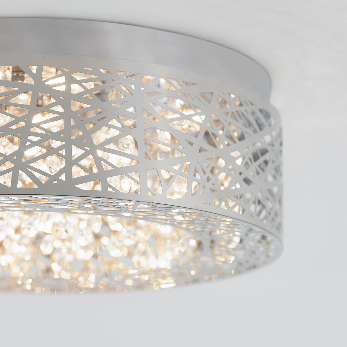 A close-up of a modern ceiling light fixture with a silver metal shade featuring an abstract cut-out pattern, allowing light to shine through and create a sparkling effect.