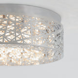 A close-up of a modern ceiling light fixture with a silver metal shade featuring an abstract cut-out pattern, allowing light to shine through and create a sparkling effect.