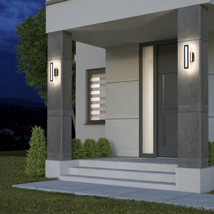 A modern house entrance at dusk features wide steps, a dark front door, neatly trimmed bushes, and two Artika Evasion modern indoor-outdoor LED wall lights (3 CCT) mounted on concrete pillars.