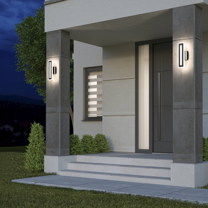 A modern house entrance at dusk features wide steps, a dark front door, neatly trimmed bushes, and two Artika Evasion modern indoor-outdoor LED wall lights (3 CCT) mounted on concrete pillars.