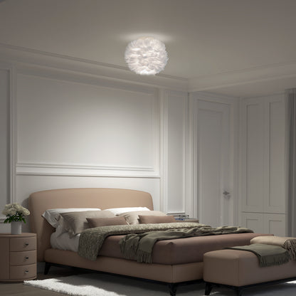 A softly lit bedroom features Artikas Plume LED flush mount light, a beige upholstered bed with green and gray bedding, a matching bench, a nightstand with flowers, and white panel-detailed walls.