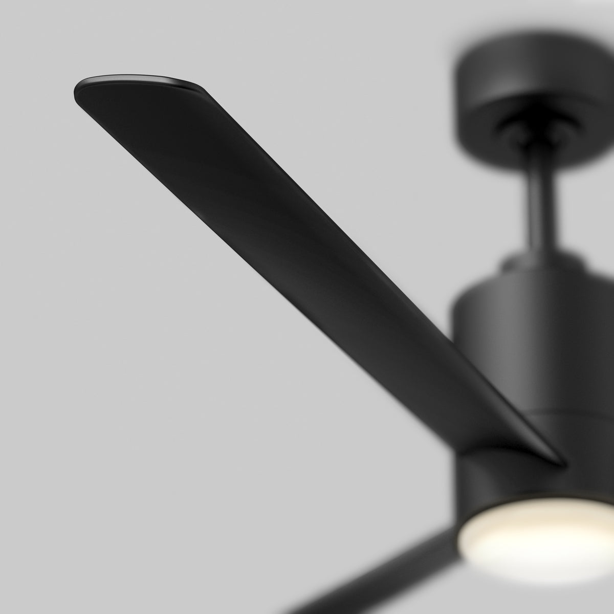 Close-up of a modern black ceiling fan with a minimalistic design, featuring a sleek blade, cylindrical motor housing, and a diffused light at the center against a plain gray background.