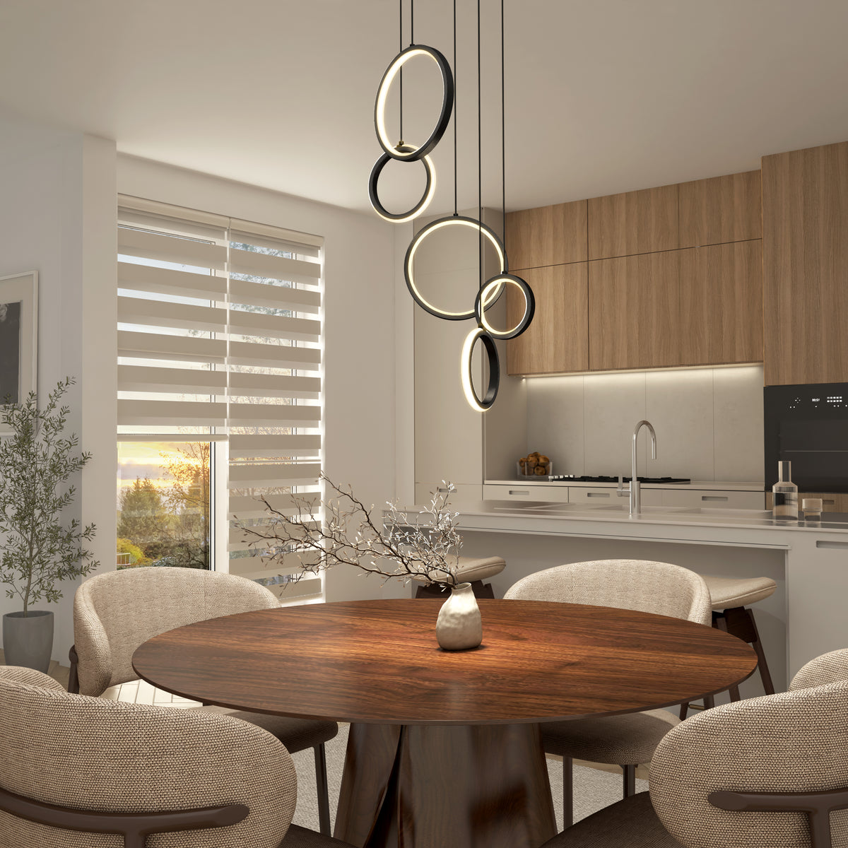 Modern dining area featuring a round wooden table, beige chairs, and the Elmo 5-light LED pendant by Artika. Kitchen with wood cabinets, built-in oven in the background, and sunlight streaming through blinds.