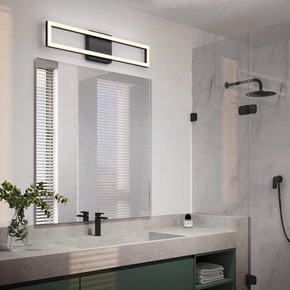 Modern bathroom with a large mirror, Artika Dover modern LED vanity light above, black fixtures, a sink with concrete countertop, glass shower featuring black showerhead, and a small vase with greenery on the counter.