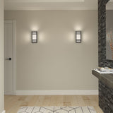 A modern, minimalist room with pale wood flooring, a geometric-patterned rug, two wall sconces emitting soft light, a white door, and a stone accent wall with a floating shelf holding decorative items.