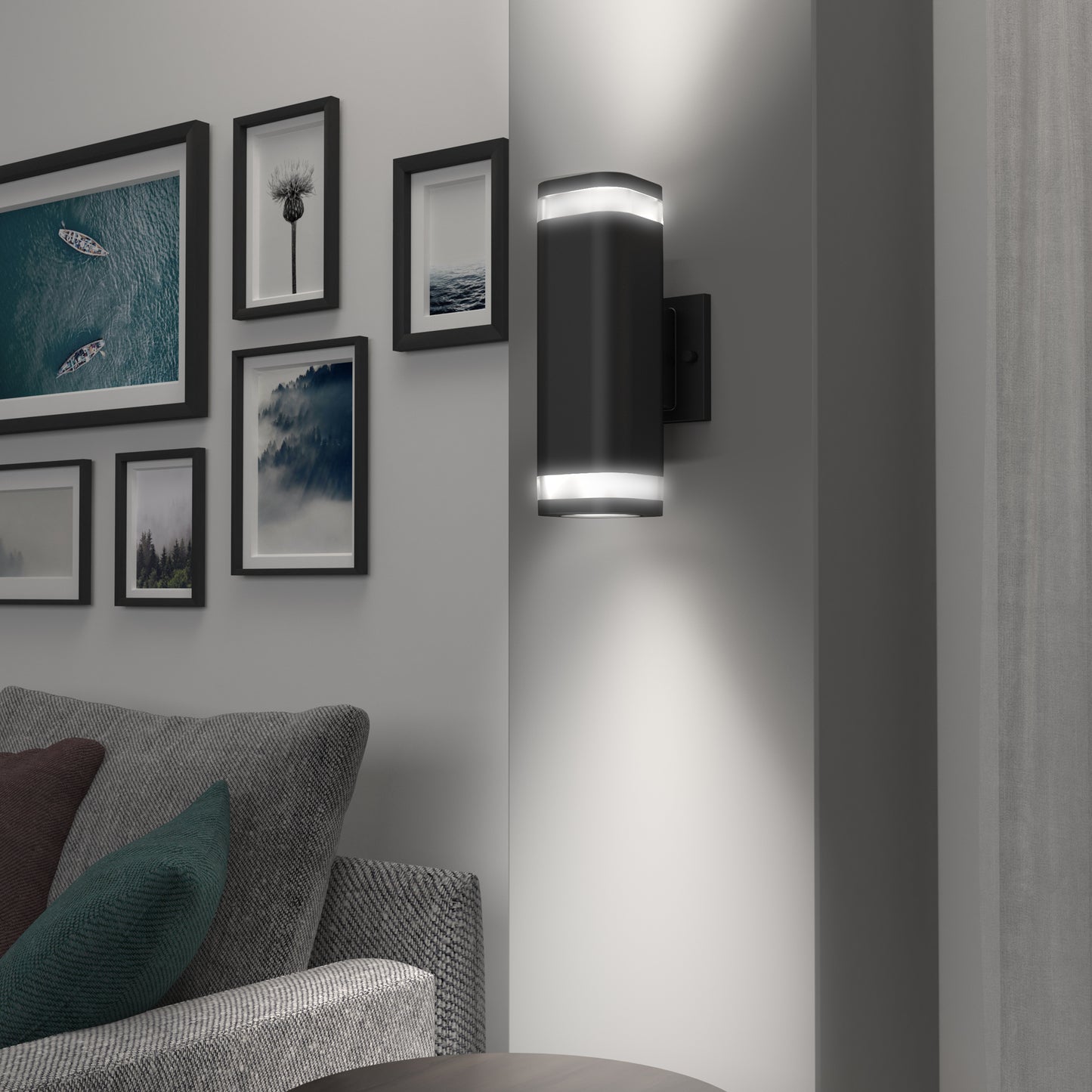 The Artika Stark modern LED indoor-outdoor light with Wi-Fi is mounted on a white wall beside a gray sofa and a gallery of framed photos, adding contemporary style and coziness to the room.