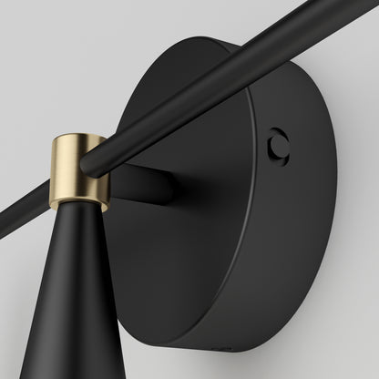 Close-up of the Artika Wayden LED mid-century bathroom vanity light 3 CCT, a modern black wall-mounted fixture with a round base, matte finish, and brass accent on the arm and shade, set against a light gray wall.