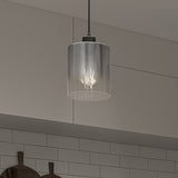 A modern pendant light with a clear glass shade and visible bulb hangs from the ceiling in a kitchen with light gray cabinets and white subway tile backsplash. Wooden cutting boards are visible on the countertop below.