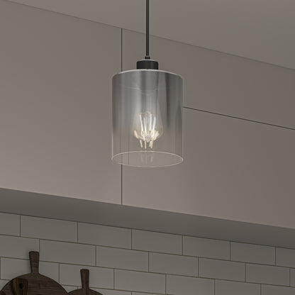 The Artika Haze pendant light with a clear glass shade and visible bulb hangs from the ceiling in a kitchen with gray cabinets and a white subway tile backsplash.