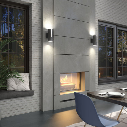Modern living space featuring Artika’s Linea modern indoor-outdoor LED wall light on a concrete wall with a double-sided fireplace, large windows, a set dining table, blue chair, and a cozy window seat with cushions and plants.