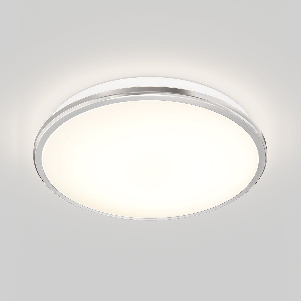A modern, round ceiling light fixture with a white diffused cover and a metallic rim, emitting a soft, even glow against a plain light gray ceiling.
