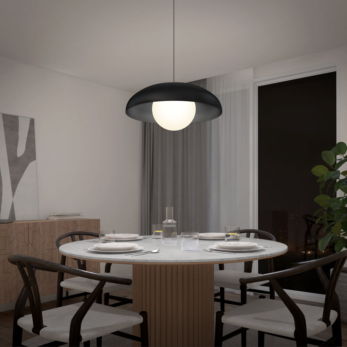 A modern dining room with a round table set for four, black chairs, a black and white pendant light overhead, a plant in the corner, large windows, and minimalist decor on the wall.