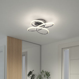 Artika's Swirl Butterfly LED contemporary flush mount light is shown installed on a white ceiling near a large mirror, wooden panel, and white door, with a green plant partially visible at the bottom.