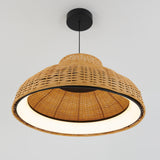A close-up view of a ceiling pendant light with a woven rattan shade and a black mount, hanging against a plain white background. The light is turned on, illuminating the inside of the shade.