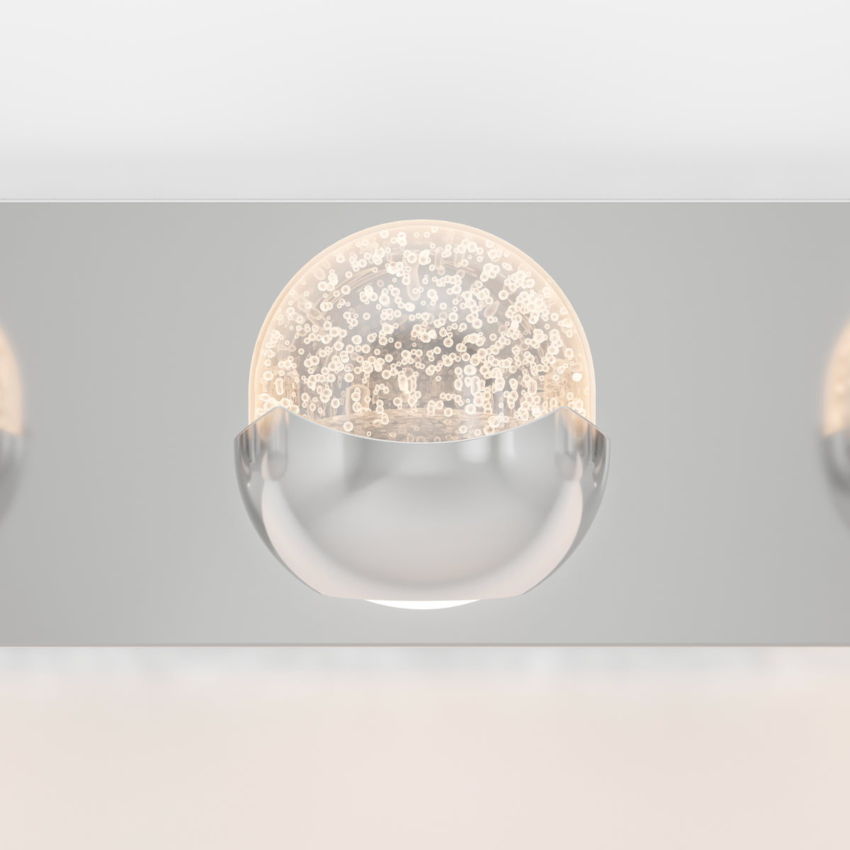 A modern light fixture with a half-globe design; the top half is a clear dome with bubble-like patterns inside, and the bottom half is smooth, reflective metal. The fixture is mounted on a sleek, metallic surface.