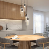 Modern kitchen with light wood cabinets, marble backsplash, and round wooden dining table set with four gray chairs. Pendant lights hang above the table; a cup and saucer rest on the table. Soft natural light fills the room.
