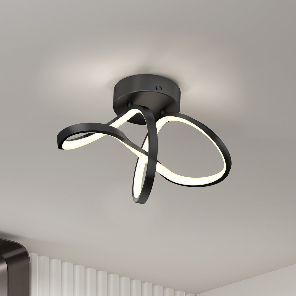 A modern ceiling light fixture with black, curved LED strips arranged in an abstract, looping design, mounted on a white ceiling in a contemporary room.