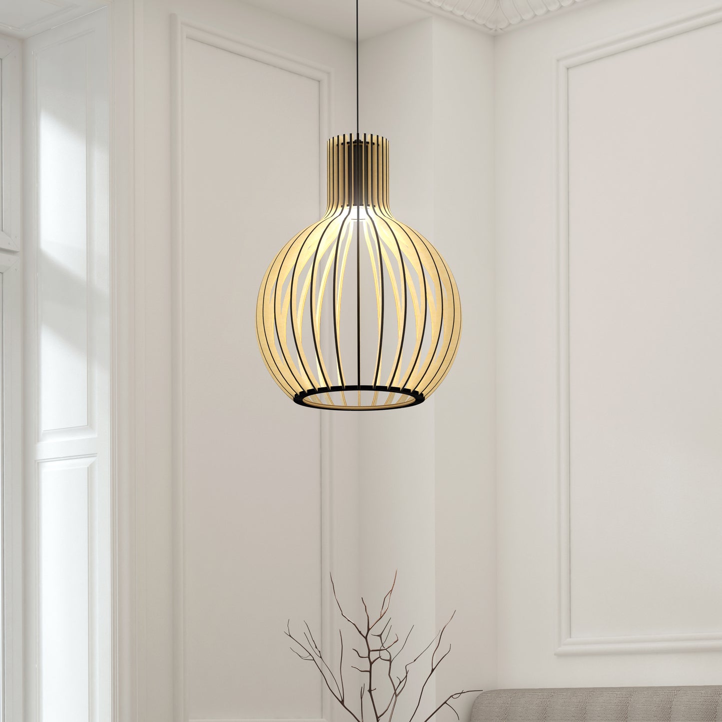 The Artika Tomi LED Pendant Light 3 CCT, featuring a modern spherical black metal frame, hangs in a bright minimalist room with white walls and wainscoting. A bare branch decor is placed below the fixture.