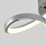 Close-up of a modern, curved LED wall light with a metallic silver finish and a glowing white strip along the inner edge, mounted against a plain light gray background.