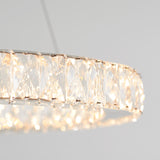 A close-up of the Celebrity LED pendant light by Artika, featuring a round design with geometric faceted crystal panels, casting a soft, warm glow against a plain light gray background.