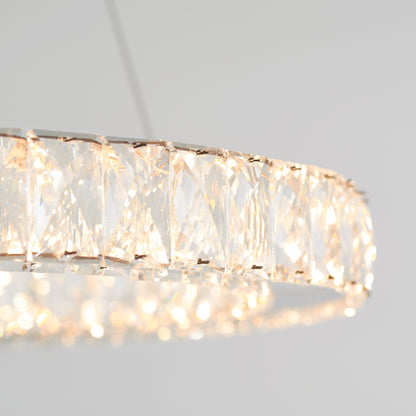 A close-up of the Celebrity LED pendant light by Artika, featuring a round design with geometric faceted crystal panels, casting a soft, warm glow against a plain light gray background.