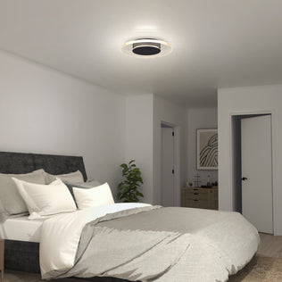 A modern bedroom features a gray upholstered bed, white and gray bedding, a small plant, a dresser with décor, and the Artika Essence Disk LED flush mount ceiling light. The walls and doors are painted white.