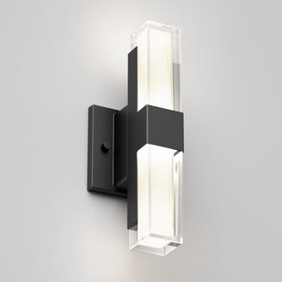 The Artika Gemini indoor-outdoor LED wall light features a black rectangular base and a vertical fixture with frosted and clear sections, mounted on a white wall to emit a soft, inviting glow.