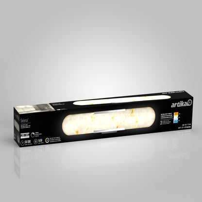 A rectangular black box labeled Selena 3 CCT LED bathroom vanity light by Artika contains a white marbled LED fixture. The packaging notes 1950 lumens, 50,000 hours lifespan, and adjustable color temperature.