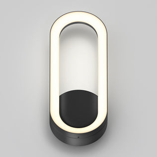 The Artika Aiden modern LED indoor-outdoor wall light 5 CCT features an oval design with a glowing white LED ring and a matte black base, shown mounted on a light gray background.
