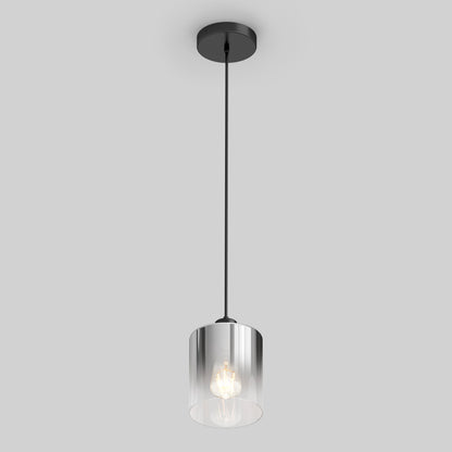 The Artika Haze pendant light glass features a modern design with a black ceiling mount and cable, a cylindrical clear glass shade, and an exposed bulb, all set against a plain light gray background.