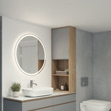 A modern bathroom with a round, illuminated mirror above a sink, a faucet, a small potted plant, and wooden shelves holding towels and toiletries next to a wall-mounted toilet.