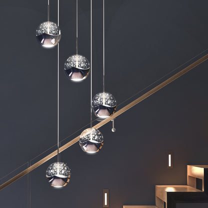 The Oracle modern 5-light LED pendant by Artika-CAN-dev features sleek, reflective spheres suspended at varying heights above a staircase with dark walls and step lights, adding a contemporary and elegant touch.