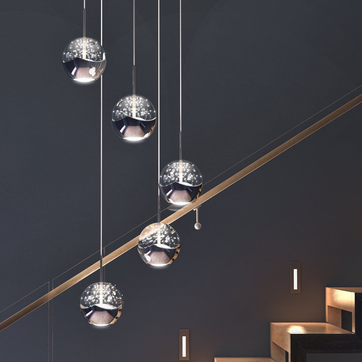 Five modern spherical pendant lights with reflective surfaces hang at varying heights beside a staircase with built-in step lights, set against a dark, minimalist wall.
