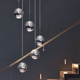 Five modern spherical pendant lights with reflective surfaces hang at varying heights beside a staircase with built-in step lights, set against a dark, minimalist wall.