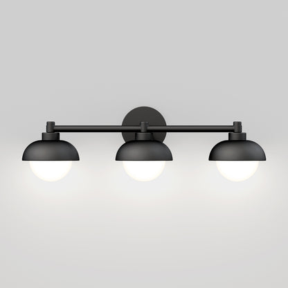 The Artika Boden LED mid-century bathroom vanity light features a black wall-mounted design with three dome-shaped shades, each housing a glowing round bulb, set against a plain light gray background.