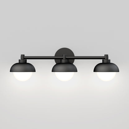 The Artika Boden LED mid-century bathroom vanity light features three black, dome-shaped shades with white glowing bulbs, wall-mounted against a plain light gray background.