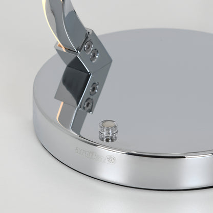 A close-up of the shiny Swirl LED table lamp’s chrome base shows a small clear button and the engraved Artika brand name with its logo on the side.