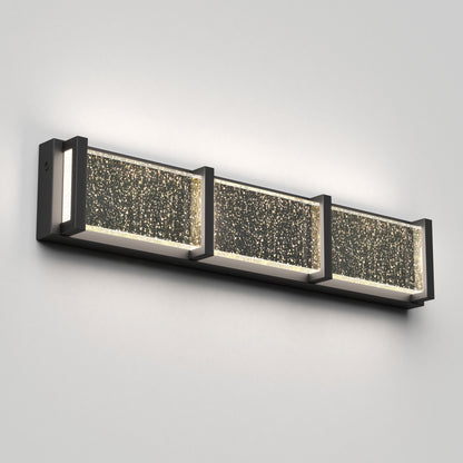 The Artika Subway Essence 3 LED bathroom vanity light features a sleek dark metal frame and three rectangular bubble glass panels, emitting warm, diffused light. This modern wall-mounted fixture is shown on a light-colored wall.