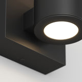 A close-up of a modern, black wall-mounted cylindrical light fixture turned on, casting a bright white light against a neutral background.