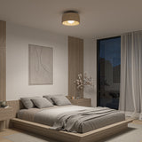 A modern, minimalist bedroom with a low wooden bed, gray bedding, two nightstands, a large window with sheer curtains, artwork on the wall, and a ceiling light. Night sky is visible outside.