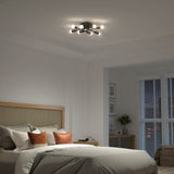 A modern bedroom with a neatly made bed, brown and white pillows, a cane headboard, and a contemporary ceiling light fixture. In the background, there’s a window with blinds and a small table with a plant.