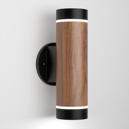 The Artika C7 indoor-outdoor LED wall light 3 CCT features a cylindrical design with a wood grain finish, black end caps, top and bottom lighting, and is mounted on a round black wall plate against a white background.