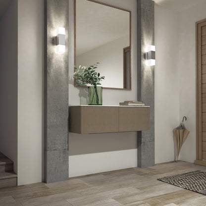 Modern entryway with light wood flooring, a floating console topped with a green vase of leafy branches, a large mirror, woven mat, umbrella stand, and two Artika Lennox indoor-outdoor LED wall lights (3 CCT) in matte black beside the stairs.