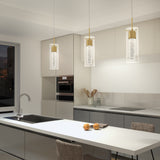 Modern kitchen with neutral tones, featuring a white island, gray cabinets, built-in oven, and three pendant lights hanging above the island. Two apples sit on the counter, and a chair is placed at the island.